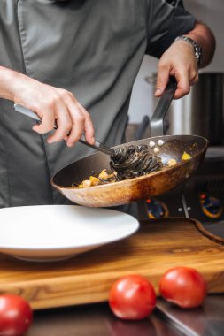 Şef tavada siyah spagetti pişiriyor.