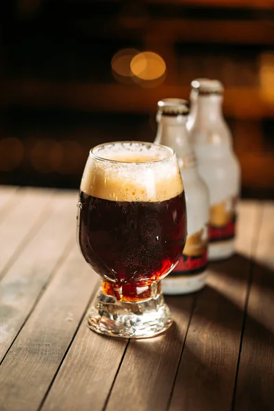 Glass with a dark foamed beer on the wooden table