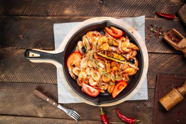 Tahtadaki dökme demir tavada kızarmış karidesler.