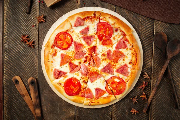 Pizza z szynką i pomidorami na drewnianym stole — Zdjęcie stockowe