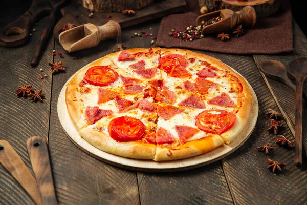Pizza with ham and tomatoes on the wooden table