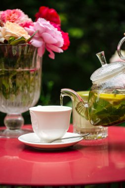 Masaya güllerle beyaz bardakta yeşil çay dök.