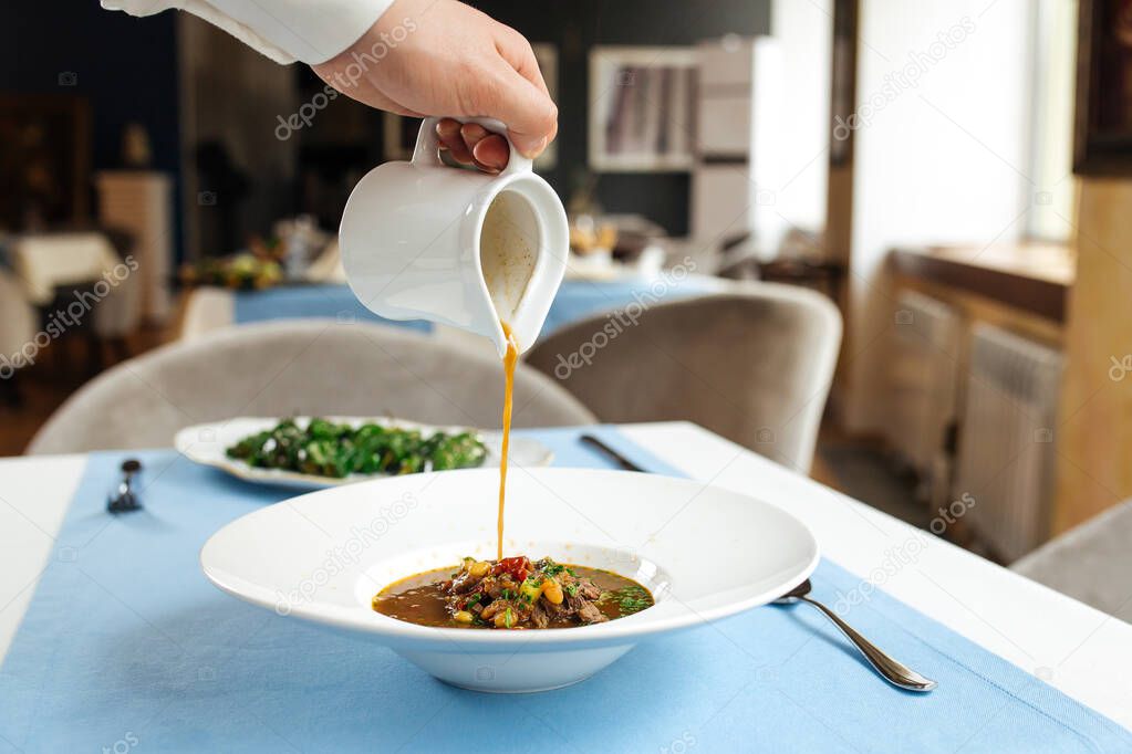 Pouring broth in a plate with spanish oxtail soup