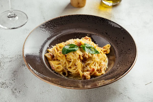 Klasik İtalyan carbonara makarnası, domuz pastırması, parmesan ve fesleğen, koyu bir tabakta servis edilir.