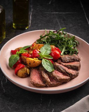 Kızarmış patatesli ızgara biftek dilimleri, kiraz domatesleri ve taze roka salatası.