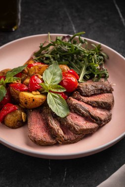 Kızarmış patatesli ızgara biftek dilimleri, kiraz domatesleri ve taze roka salatası.