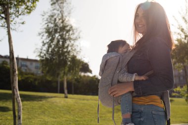 Genç anne küçük yürümeye başlayan çocuk taşıyan bir park üzerine 