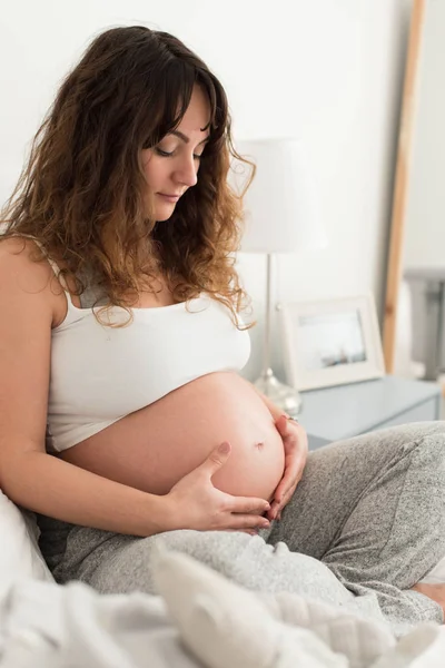 快乐的孕妇坐在家里抚摸她的肚子 — 图库照片