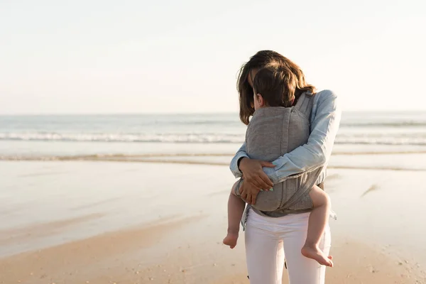 母亲带着 Ergobaby 在沙滩上抱着孩子 — 图库照片