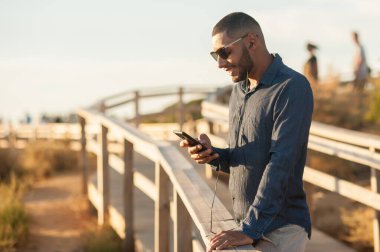 Latin bir adam gün batımı manzarası için akıllı telefonuyla mesaj atıyor. Doğal açık hava ışığı