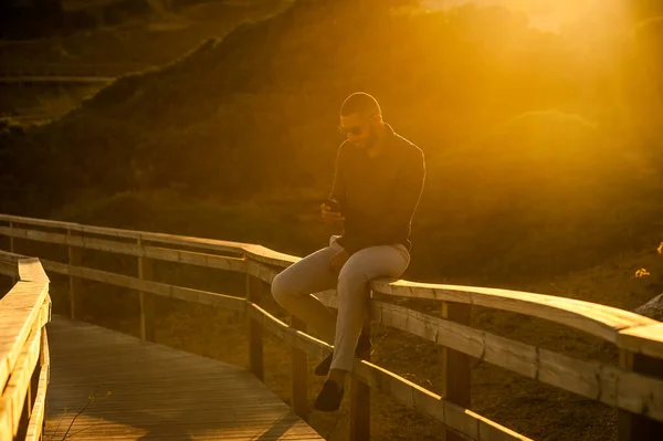 拉丁男人用智能手机在日落美景中发短信 自然室外照明 — 图库照片
