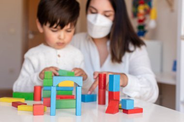 Liltle Anaokulu Çocuğu tahta bloklarla oynuyor ve öğretmen eğitmeni koronavirüs salgını için yüz maskesi kullanıyor. Ev hapsi. Öğrenme Topluluğu. Montessori Schoo