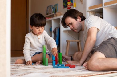 Küçük çocuk ve babası evde tahta bloklarla oynuyorlar. Evde eğitim. Evde kal. Aile zamanı.