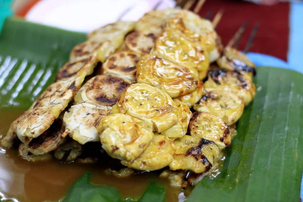 Grilled banana with dipping sauce on wooden table.