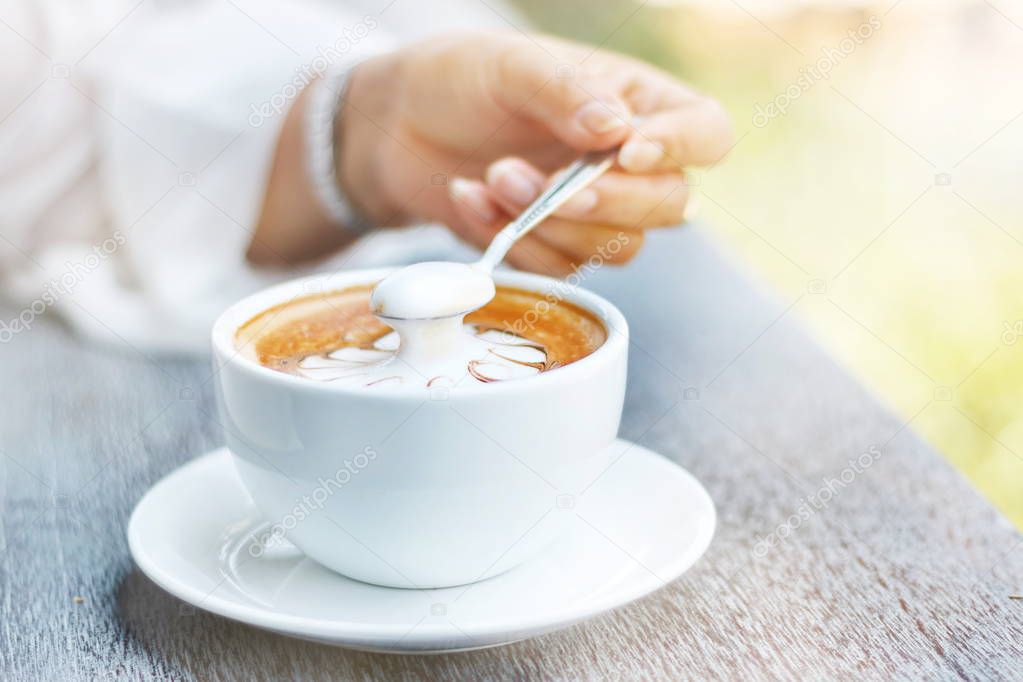 Hands are holding a cup of hot latte coffee on a natural blurred background.