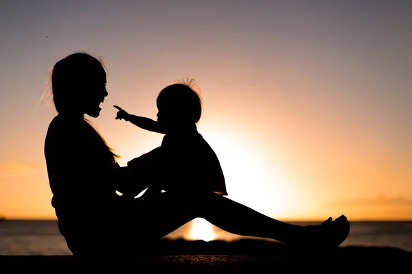 Mère et enfant jouant et regardant coucher de soleil sur la plage en silhouette — Photo