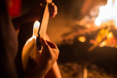Dışarıda gitar çalan bir bayan müzisyen, ateşin yanında oturuyor. Rahatlama.