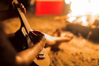 Sahilde bir kamp ateşi yanında gitar gitar çalmak bir müzisyen kadın.
