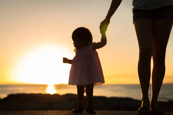 Petite fille regardant le coucher du soleil avec sa mère sur la plage. Silhouette . — Photo