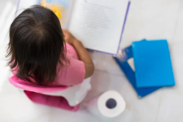 Potty training. Toddler sitting on the toilet reading a book.