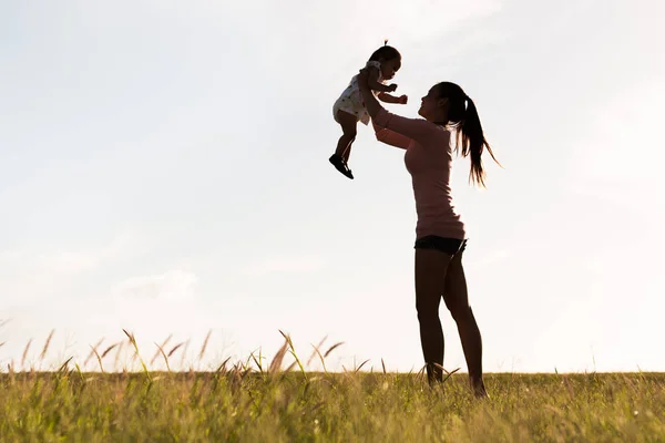 Uma mãe feliz levantando seu bebê no ar livre . — Fotografia de Stock