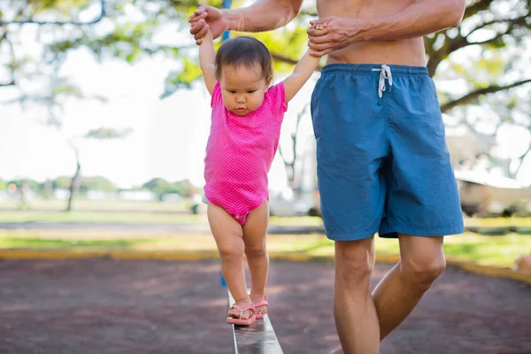 Un père aidant son enfant à marcher, en équilibre sur un obstacle de terrain de jeu . — Photo
