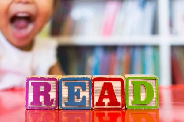 Alphabet blocks spelling the word read in front of a bookshelf and an excited child in the background