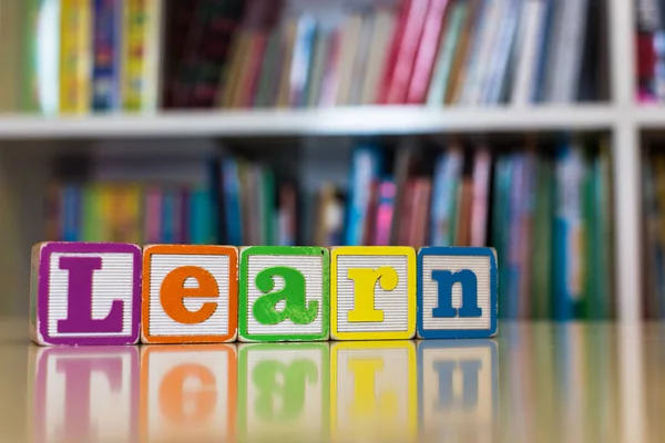 Alphabet blocks spelling the word learn in front of a bookshelf