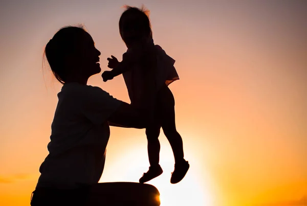 Silhueta de uma mãe segurando seu bebê na frente de um pôr do sol — Fotografia de Stock