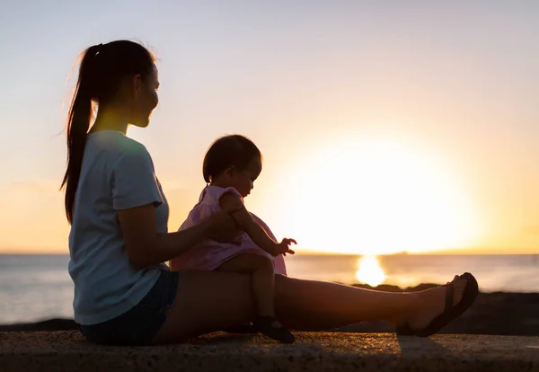 Mãe com seu bebê sentado em seu colo assistindo o pôr do sol — Fotografia de Stock