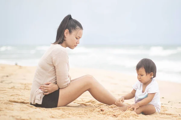 Üzgün bir kadın kumsalda oynayan bebeğine bakar. — Stok fotoğraf
