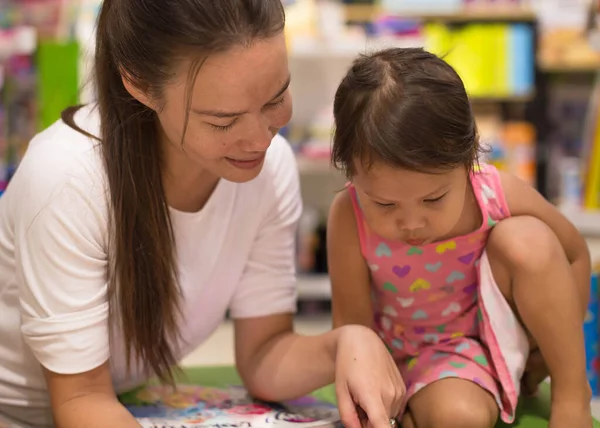 Madre está felizmente leyendo un libro a su hija en la librería — Foto de Stock