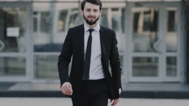 Genç işadamı kamera ve kamera, arka plan iş merkezi gülümseyen, sonra ayakta ve mutlu seyir için düz yürüyüş.