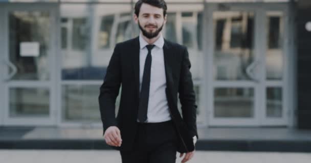 Young businessman walking straight to the camera and smiling, then standing and happy looking to the camera, background business center. — Stock Video