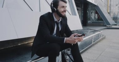 Genç yakışıklı iş adamı bir takım elbise telefonunu kullanarak iş merkezi önünde müzik dinleme.