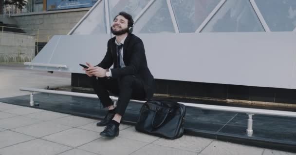 Al lado del centro moderno joven hombre de negocios en un traje escuchar música desde los auriculares — Vídeos de Stock