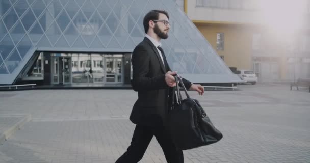 Elegante hombre de negocios caminando por el centro de negocios sosteniendo su maletín — Vídeo de stock