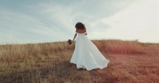 Mariée en cours d'exécution en robe longue incroyable à travers le paysage . — Video