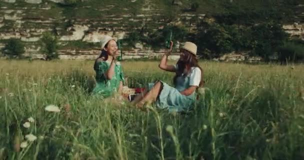 Dos chicas guapas con sombreros tienen un gran tiempo de picnic beber cerveza y pasar buen final de semana . — Vídeos de Stock