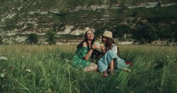Dos chicas jóvenes tienen un tiempo de picnic comiendo sándwiches y Loy directamente a la cámara tienen una cara sonriente — Vídeos de Stock