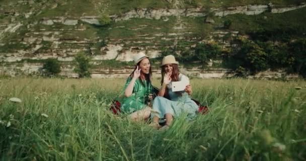 Dwie dziewczyny niesamowite mieć piknik razem i za pomocą tabletu, mówiąc z kimś szczęśliwa i uśmiechnięta, dając cześć — Wideo stockowe
