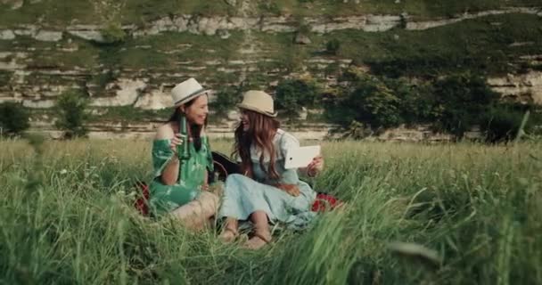 Dos chicas sonrientes bastante felices usando la tableta en su hora de picnic. 4k — Vídeo de stock