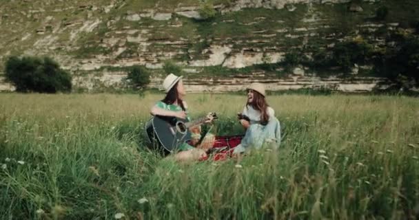 Пікнік час з двома дівчатами, які співають на гітарі і другій дівчині роблять фотографії, вони щасливо посміхаються. 4k — стокове відео