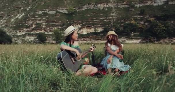 Lächelnde hübsche Mädchen picknicken, singen an der Gitarre und haben eine tolle Zeit zusammen. — Stockvideo