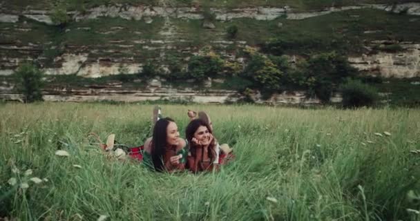 Duas meninas no meio da grama deitado no cobertor e passar um bom tempo juntos no piquenique — Vídeo de Stock