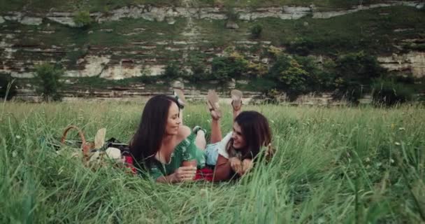 No meio da grama verde duas meninas bonitas deitado e ter um piquenique, passar um bom tempo juntos — Vídeo de Stock