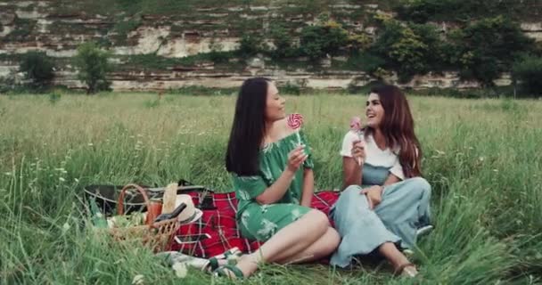 Tiempo de picnic con dos chicas en medio de la montaña, tener dos piruletas y feliz sonrisa . — Vídeo de stock