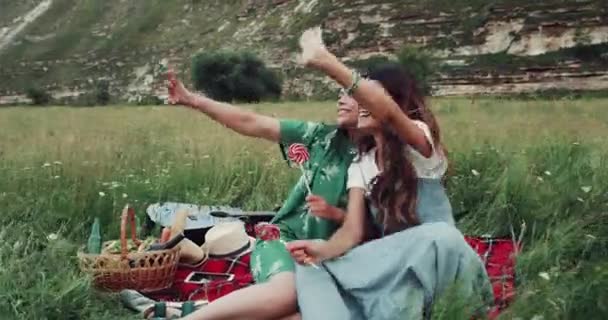 Due giovani ragazze hanno un tempo pic-nic, mangiare lecca-lecca e dare ciao a qualcuno . — Video Stock