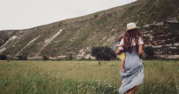 Young girl with her baby boy walking through the grass looking around , in the middle of mountain — Stock Video