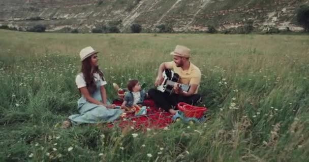 Piquenique incrível com uma família, no meio da natureza, o homem está tocando na guitarra — Vídeo de Stock